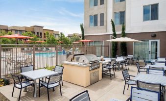 an outdoor dining area with tables , chairs , and umbrellas near a swimming pool , surrounded by buildings at Homewood Suites by Hilton Aliso Viejo Laguna Beach