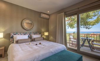 a bedroom with a large bed , a mirror on the wall , and a view of the ocean through a sliding glass door at Koukounaria Hotel & Suites