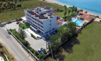 an aerial view of a hotel with a pool and ocean in the background , surrounded by grass and trees at Poseidon Beach Hotel