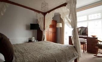 a cozy bedroom with a four - poster bed draped in a lace canopy , creating a warm and inviting atmosphere at The Bugle Coaching Inn