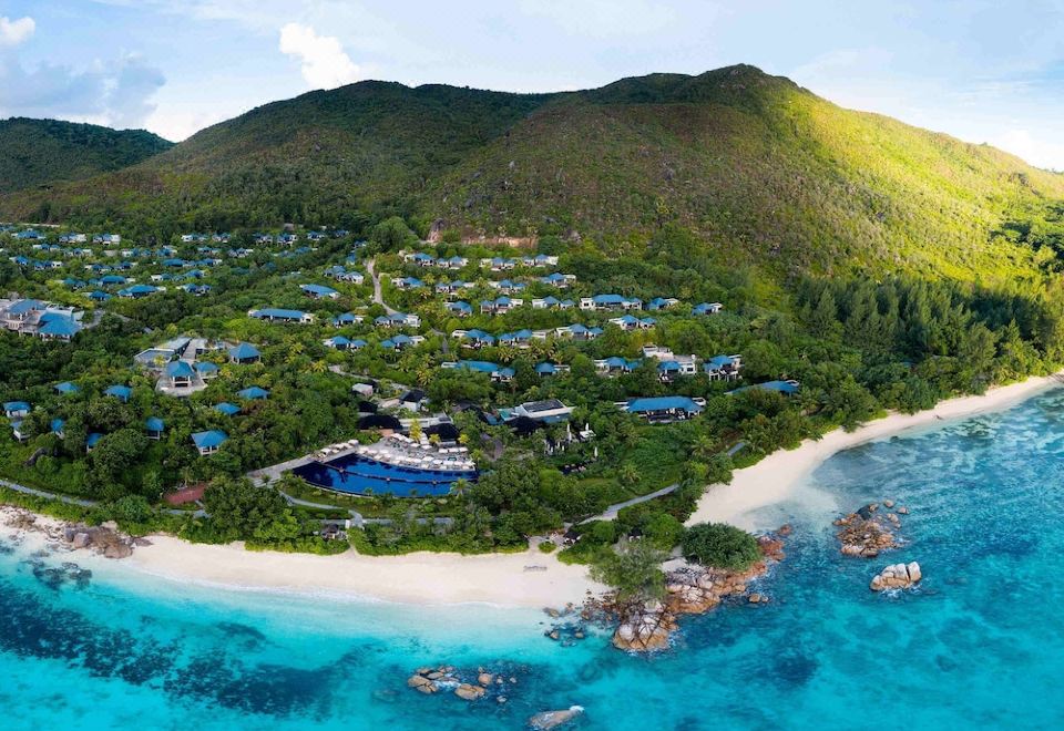 a bird 's eye view of a resort with blue pools , surrounded by trees and mountains at Raffles Seychelles