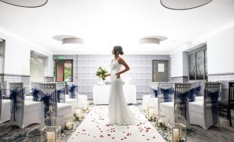 a bride in a white dress standing in front of a wedding arch decorated with rose petals at Birch Hotel
