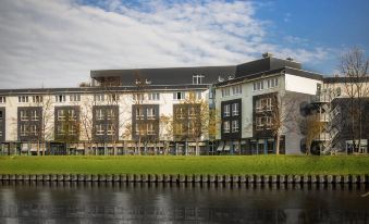 a large building with a brick facade is situated next to a body of water at Ginn Hotel Berlin Potsdam