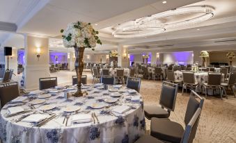 a large banquet hall with multiple round tables covered in blue and white tablecloths , surrounded by chairs at The Kingsley Bloomfield Hills - a DoubleTree by Hilton