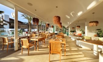 a spacious , well - lit dining room with wooden tables and chairs arranged for a group of people at Hard Rock Hotel Tenerife