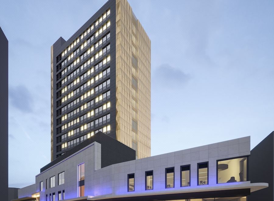 a modern building with a large glass window and a stone wall is surrounded by people at Mercure Newport