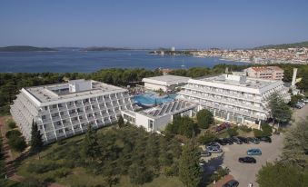 a large white hotel complex with multiple buildings and a body of water in the background at Hotel Olympia