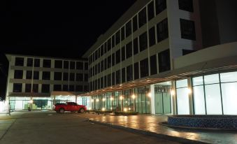 a modern building with multiple floors and large windows , illuminated by lights at night , with cars parked outside in the foreground at Klongyai Center