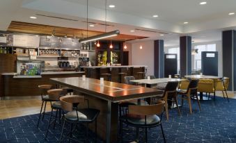 a modern restaurant with wooden tables and chairs , a bar , and a blue carpet on the floor at Courtyard Columbus New Albany