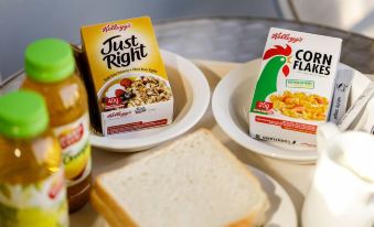 a dining table with a variety of food items , including two boxes of cereal , a bottle of juice , and a sandwich at Valley View Motel