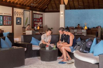 a group of people , including a man and two women , are sitting on a couch in a room , enjoying each other 's company at Vilamendhoo Island Resort & Spa