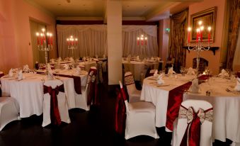 a formal dining room with tables covered in white tablecloths and adorned with red napkins at The Imperial Hotel