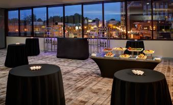 a room with tables and chairs , a table with food on it , and a large window overlooking a cityscape at Marriott East Lansing at University Place