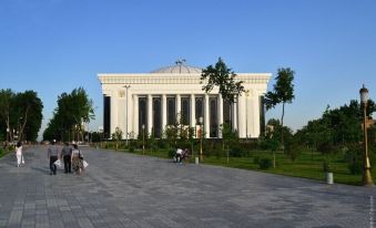 a large white building with columns and a central dome , surrounded by people walking on a paved walkway at Orion Hotel