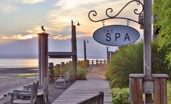 a sign for the spa is hanging from a metal railing overlooking a beach and water at The Inn at Langley