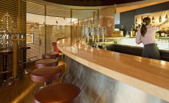 a bar with a wooden counter and stools , where several bottles of alcohol are displayed at Novotel Leuven Centrum