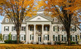 a large white house with columns and a green awning is surrounded by trees in the fall season at Rochester Airport Marriott