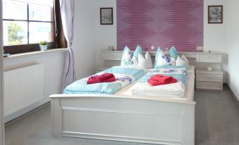 a white bed with blue and pink bedding in a bedroom with a purple accent wall at Petra