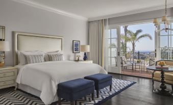 a large bedroom with a white bed , blue ottoman , and sliding glass doors leading to a balcony at Rosewood Miramar Beach