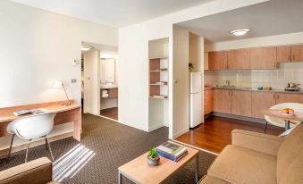 a modern living room with a couch , coffee table , and kitchen in the background at Ibis Melbourne Hotel and Apartments