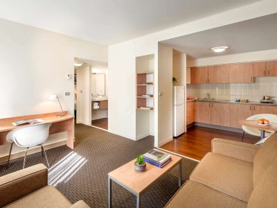 a living room with a couch , coffee table , and kitchen in the background , along with a kitchen in the foreground at Ibis Melbourne Hotel and Apartments