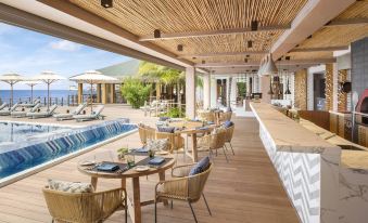 an outdoor dining area with a long wooden table , several chairs , and a pool in the background at JW Marriott Maldives Resort & Spa