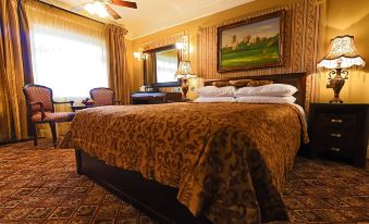 a large bed with a brown blanket is in a room with two lamps and paintings on the walls at Riverside Inn