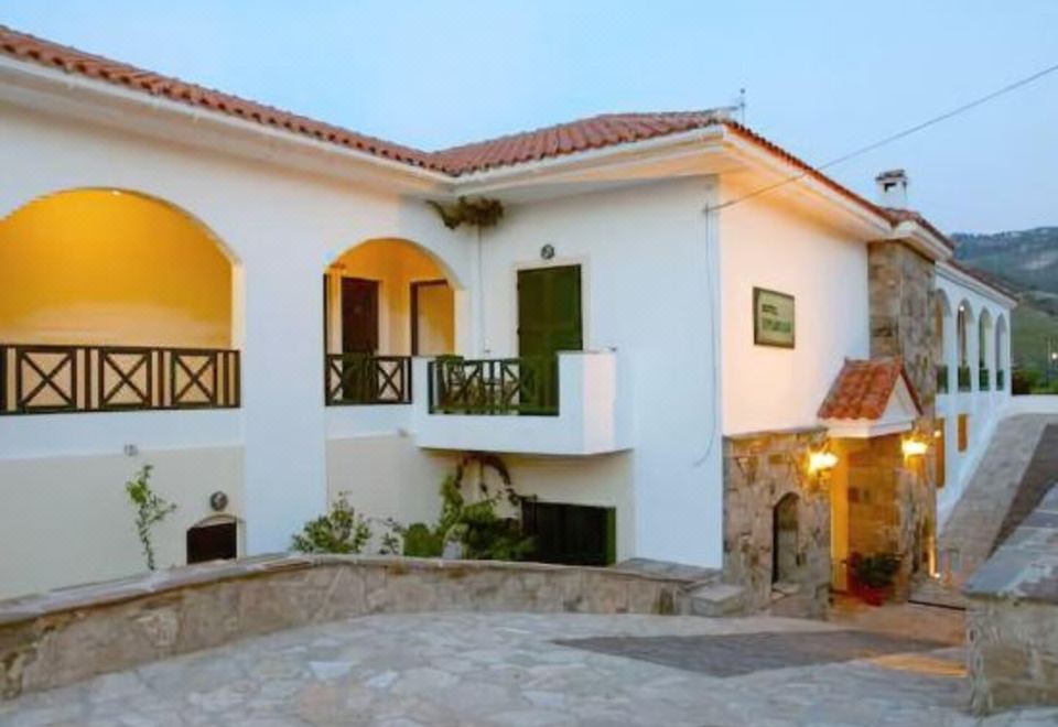 a two - story house with a red tile roof and white walls , situated on a stone walkway at Erofili Beach Hotel