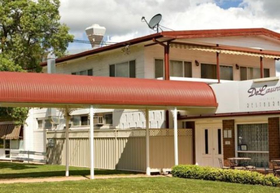 a red - roofed building with a satellite dish on the roof , and a grassy area in front at Cherry Blossom Motor Inn