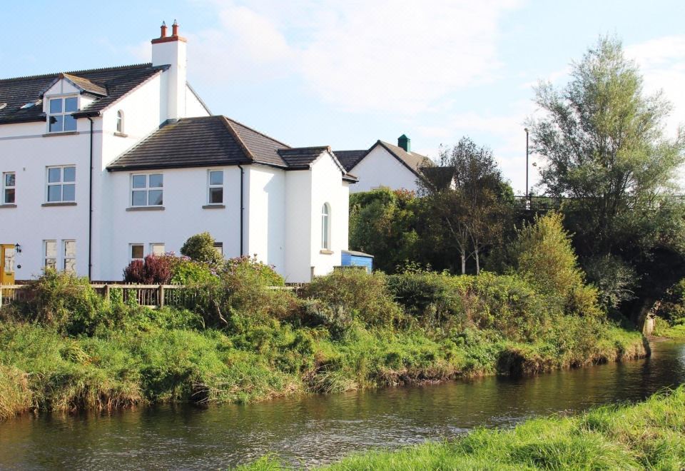 a white house is situated next to a river , with trees and grass surrounding it at Maison