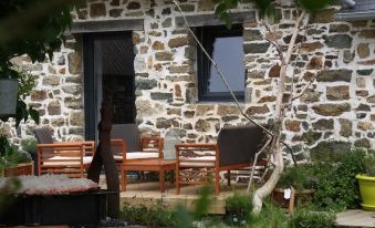 a stone house with a wooden patio area featuring a table , chairs , and a bench at La Vieille Ferme
