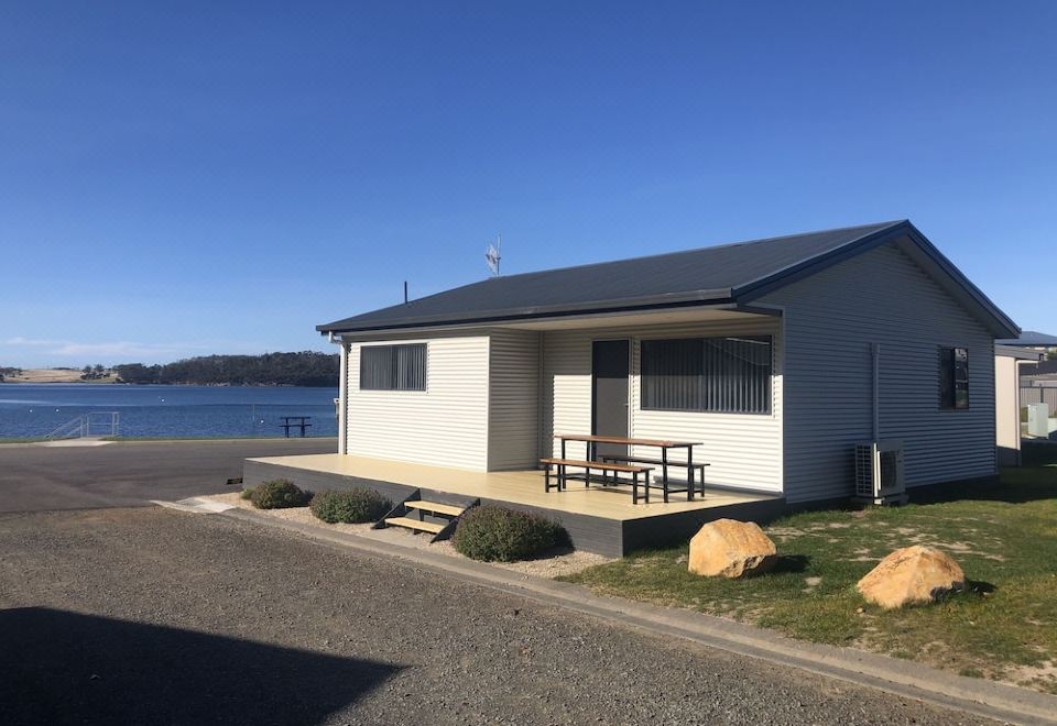 a white house with a deck and picnic table is situated on the shore of a lake at Eastcoaster Tasmania