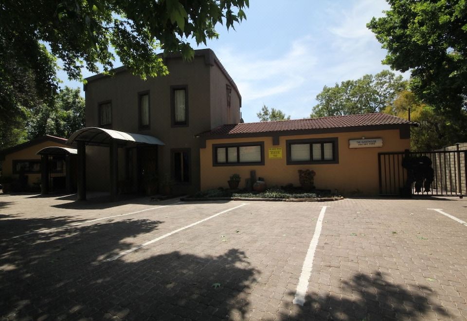 a brick building with a brown roof , situated on a parking lot in front of a tree at The Guesthouse