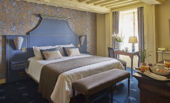 a luxurious hotel room with a large bed , blue and gold wallpaper , and a bench at the foot of the bed at Chateau d'Audrieu