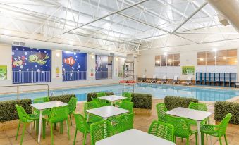 an indoor swimming pool area with tables , chairs , and a mural on the wall , surrounded by a large open space at North Devon Resort