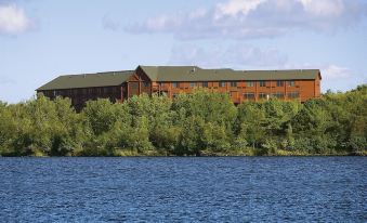 a large building with a green roof and multiple windows is surrounded by trees and water at Grand Ely Lodge