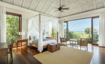 a luxurious bedroom with a canopy bed , wooden floors , and a view of the ocean through large windows at Como Parrot Cay