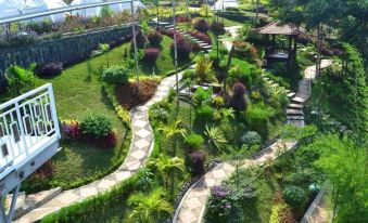 a winding path leads through a lush green garden with various plants and trees , surrounded by buildings at Chevilly Resort & Camp