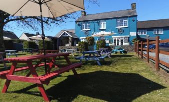 a blue house surrounded by a grassy yard , with several picnic tables and umbrellas in the area at Parsonage Farm Inn