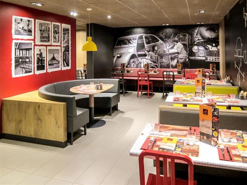 a restaurant with a red and yellow theme , featuring a round dining table surrounded by chairs at Ibis Lyon Villefranche Sur Saone