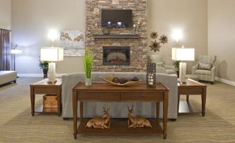 a cozy living room with a stone fireplace , wooden furniture , and two deer figurines on a table at Grandstay Hotel Suites Thief River Falls