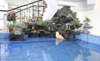 a blue tiled swimming pool with a waterfall feature and plants , set against a white wall at Sao Mai Hotel