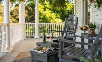 a porch with two rocking chairs , one on the left and one on the right , and a wine bottle on a table at The Jacqueline House of Wilmington