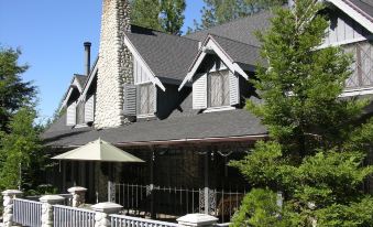 a large house with a gray roof and white railings is surrounded by trees and has an umbrella on the porch at The Creekstone