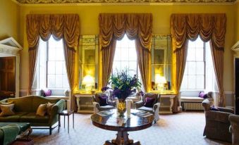 a spacious living room with yellow walls , large windows , and various pieces of furniture such as a couch , chairs , and a coffee table at Ston Easton Park