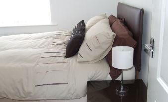 a bed with a brown headboard and white sheets is next to a nightstand with a lamp at Railway House