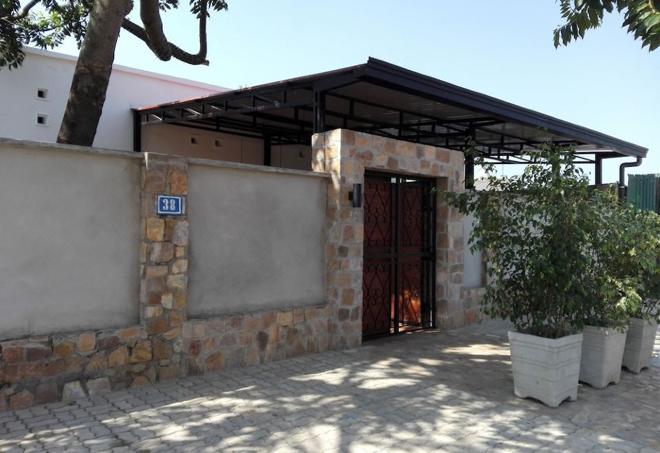 a small stone house with a covered entrance , surrounded by a paved courtyard and trees at Urban Lodge