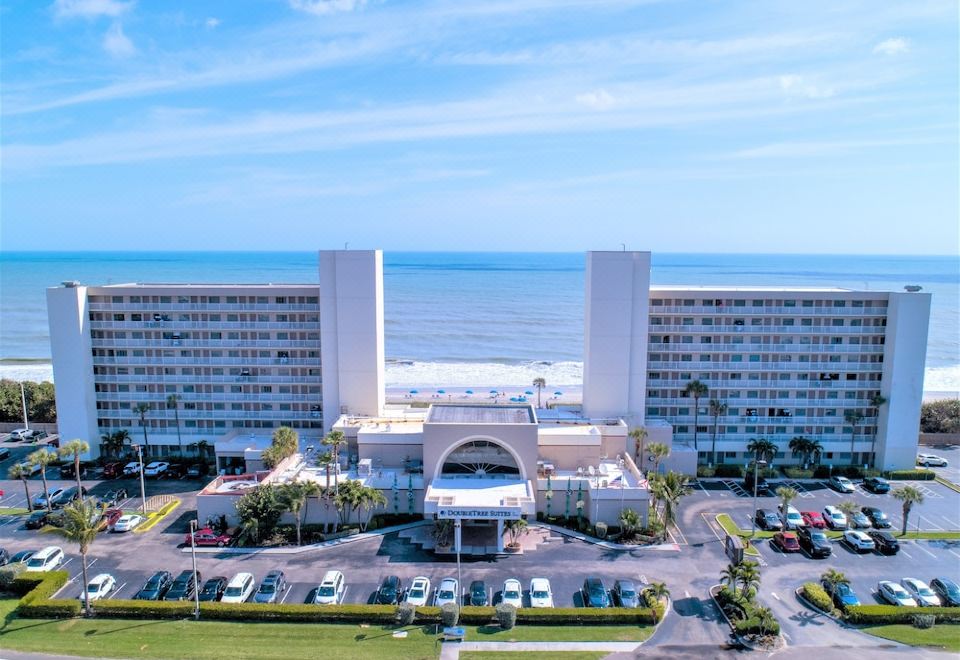 an aerial view of a large building with a parking lot and ocean in the background at DoubleTree Suites by Hilton Melbourne Beach Oceanfront