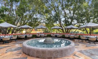 a beautiful outdoor setting with a large fountain in the center , surrounded by tables and umbrellas at Hotel Rancho San Diego Grand Spa Resort