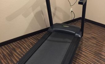 a black treadmill with a digital display is positioned against a beige wall , which appears to be in use at Cobblestone Inn & Suites - Holstein